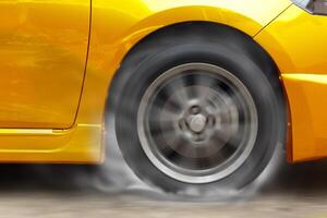 Gold car racing spinning wheel burns rubber on floor. photo