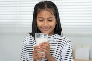 los niños las mujeres beben leche para nutrir el cuerpo y nutrir el cerebro. una niña asiática aprende en casa. niña feliz bebe leche y lee un libro para el examen, educación en el hogar. educación, vitaminas, desarrollo foto