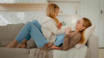 Caucasian relaxed mother and cute small child daughter having fun smiling lying on sofa smile funny mum enjoying bonding communication spending time with little funny kid baby at home happy family photo