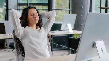 Young attractive hispanic woman office manager businesswoman typing on computer carefree female professional worker finishes work leans back on back chair puts hands behind head relaxing enjoying rest photo