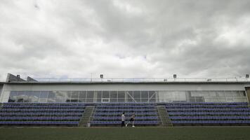 Sports field with training athletes with empty seats and cloudy sky on the background. Stock footage. Concept of olympic games, sport, and active lifestyle. photo