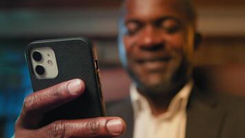 Blurred focus african american businessman holding smartphone browsing social network writing email message happy man chatting remotely communicating with client using mobile phone close-up telephone photo