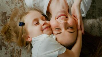 Cute affectionate adopted little kid preschool girl hugging cuddling mother head top view. Child daughter with mum two faces cuddle lying down at home talking smiling with eyes closed tender moment photo