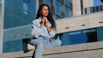 Pensive stressed sad woman girl with mobile phone sits in city near building thinks about problem looking for solutions worries about low battery gadget bad cellular communication smartphone device photo