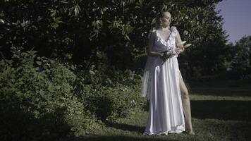 Beautiful woman in white dress on green garden background. Action. Woman in white wedding dress on sunny summer day. Beautiful bride in green garden in summer photo