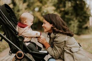 Young woman with cute baby girl in baby stroller at the autumn park photo