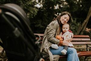 Young woman sitting on a bench with cute baby girl in the autumn park photo