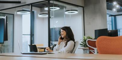 Young business woman using mobile phone while working on laptop in the modern office photo