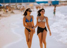 dos bonito joven mujer teniendo divertido en el playa foto