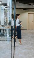 Young woman with digital tablet walking in the modern office hallway photo