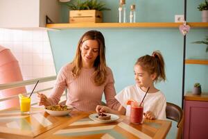 madre y hija teniendo un desayuno con Fresco exprimido jugos en el café foto