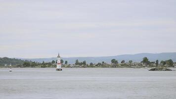 Beautiful landscape on small lighthouse in lake on background of town. Action. Lighthouse in center of river with flying gulls and shore in summer. Coastal small lighthouse near town photo