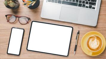 Office desk workplace with blank screen tablet and smart phone, laptop, pen, eyeglass and cup of coffee. Top view flat lay. photo