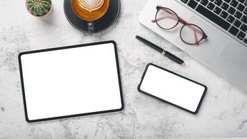 A sleek workspace featuring a tablet, smartphone, and laptop with a cup of cappuccino, glasses, and pen on a marble background. photo