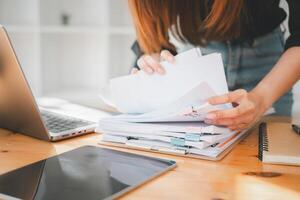 mujer de negocios trabajando en pilas de papel archivos para buscando y comprobación inconcluso documento logra en carpetas documentos a ocupado trabajo escritorio oficina. foto