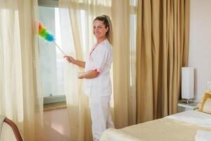 Image of beautiful hotel maid cleaning room with a duster. photo