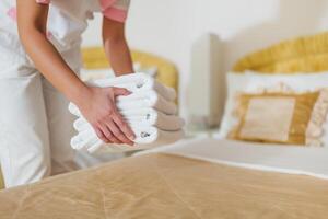 Close up image of hotel maid putting fresh and clean towels on bed. photo