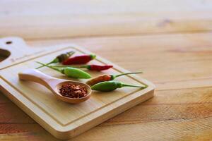 A spoon of cayenne pepper and fresh chilli on wooden background photo