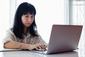 asiático mujer utilizando ordenador portátil y trabajando a hogar foto