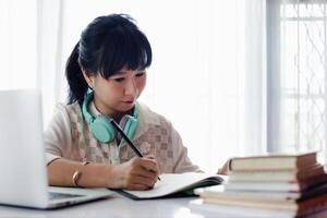 Asian woman writing on the paper, using laptop and working at home photo