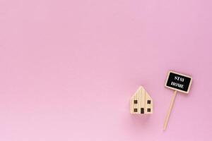 Wooden house model with stay home text on pink background photo