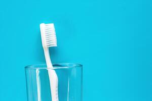 White toothbrush in the transparent glass used for cleaning the teeth on blue background photo