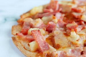 Delicious pizza with pineapple, ham slice, bacon slice, mozzarella cheese, pizza sauce on white marble background photo