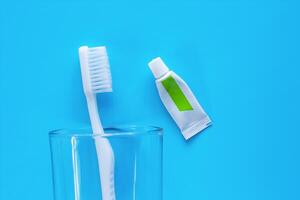 White toothbrush in the transparent glass with toothpaste used for cleaning the teeth on blue background photo