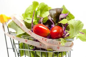 Vegetables in the shopping cart with measuring tape on white background photo