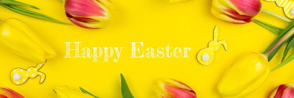 Happy easter floral banner flat lay with various bunnies and colorful tulips on yellow background. Top view. Copy space. photo