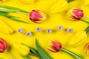 Easter floral background with colorful tulips and word easter using wooden blocks on yellow background. Top view. photo