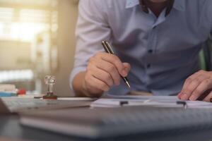 mano de hombre con pluma escribiendo en un cuaderno con computadora portátil en el escritorio. foto