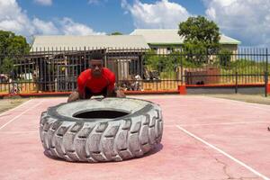 africano muscular hombre trabajando fuera en gimnasio voltear grande neumático foto