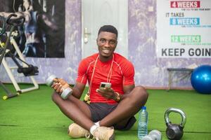 handsome african man in the holding dumbbell as he uses his phone to watch tutorials photo