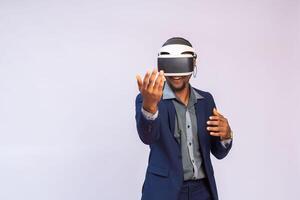 cerca arriba retrato de hermoso hombre jugando vídeo juegos en gafas de protección o 3d lentes. africano jugador vistiendo virtual realidad auriculares para inteligente teléfono en su cabeza, sonriente, en pie en contra blanco antecedentes foto