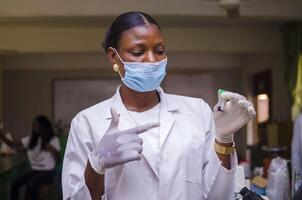 beautiful african doctor holding a bottle of COVID 19 vaccine with a hand glove photo