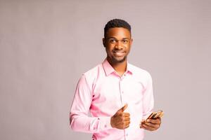Handsome excited young african business man using mobile phone isolated over gray background, wearing formal shirt, celebrating success photo