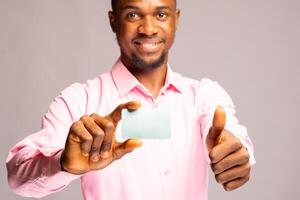 hermoso africano hombre sonriente como él sostiene es crédito tarjeta y hizo pulgares arriba foto