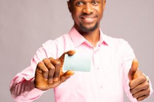 hermoso africano hombre sonriente como él sostiene es crédito tarjeta y hizo pulgares arriba foto