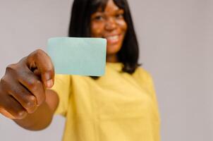 Satisfied smiling girl in stylish clothes holding bank credit card near face while standing on isolated blue background. E-banking concept photo