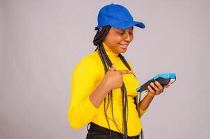 pretty black lady smiling while holding and showing a point of sale device and pointing to the device photo