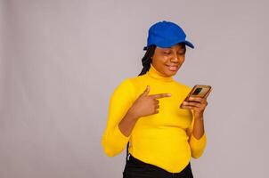 pretty lady isolated over white background wearing yellow cloth pointing to her phone photo