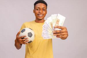 Sport Bets. Portrait Of Excited Black Guy With Football Ball And Money Standing Over Beige Background. photo
