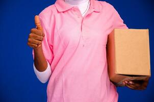 beautiful black female courier worker holding a box, does a thumbs up gesture photo