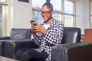 Happy female checking smart phone sitting on a couch in the living room at home photo