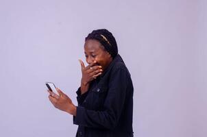 beautiful young african woman using her phone looking amazed and rejoices photo