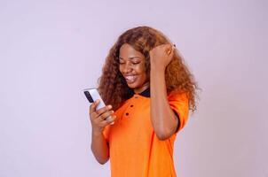 beautiful young african woman using her phone looking amazed and rejoices photo