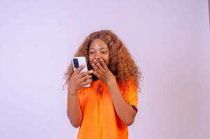 beautiful young african woman using her phone looking amazed and rejoices photo