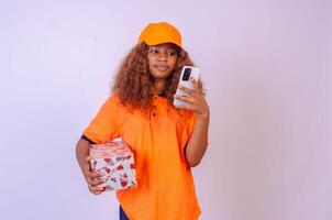 beautiful african female courier worker holding a box and using cellphone photo