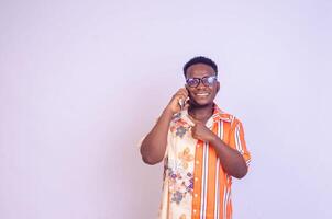 young black African boy standing on a white studio wall making calls with his mobile phone laughing out photo